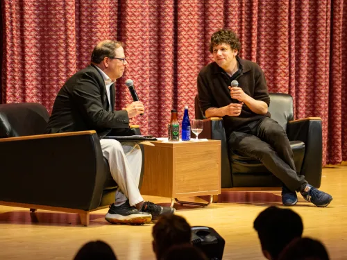 A man interviews actor Jesse Eisenberg on a stage.