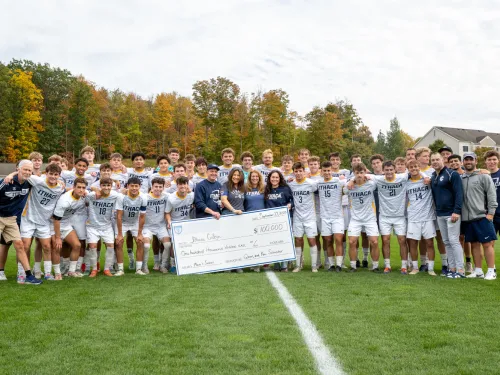 Soccer players and donors gather on a soccer pitch with a giant check.