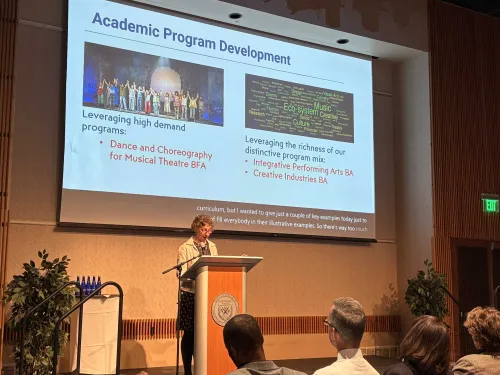 Woman stands at lectern with slides on screen behind her.