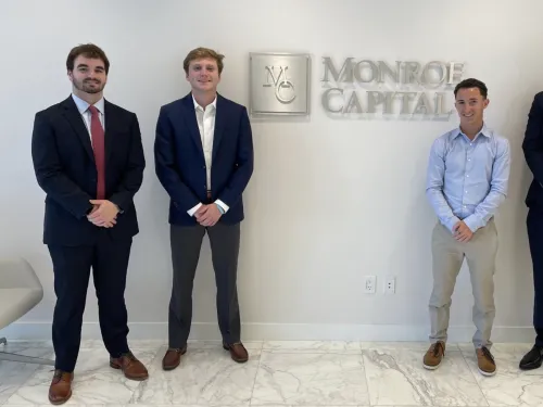 Students standing in front of wall with Monroe Capital sign