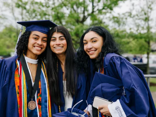 three female graduates pose together outside in caps and gowns
