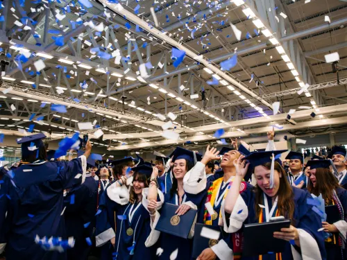 Graduates in gowns celebrate amidst confetti.