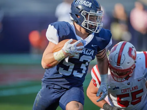 A college football player in a blue uniform evades an opposing player in a red uniform.