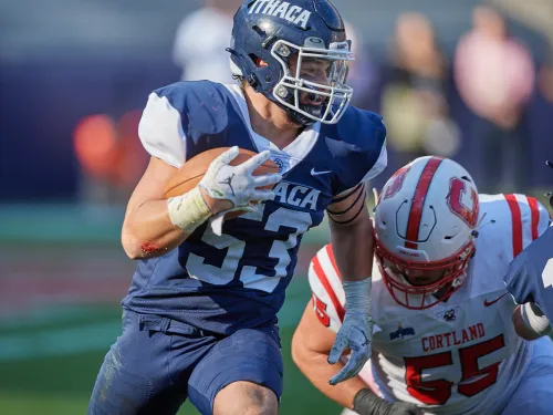 A college football player in a blue uniform evades an opposing player in a red uniform.