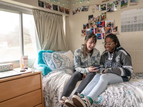 Students sitting on bed in quad residence hall.
