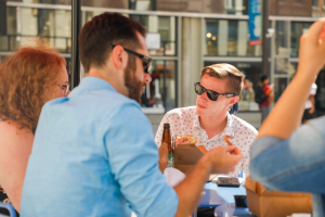 A student with sunglasses is seated at an outdoor restaurant eating with 3 other students.
