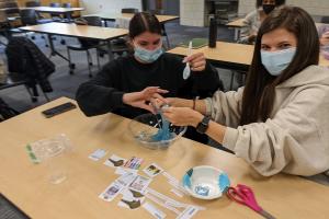 Two OT students sit at a table kneading blue toy slime in a glass bowl