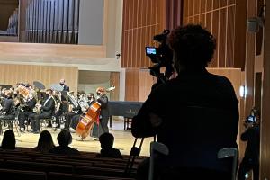 A student is seated behind a camera filming a musical performance.