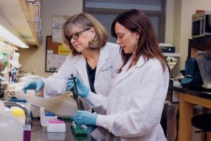 Two faculty members in lab coats work in bio safety lab