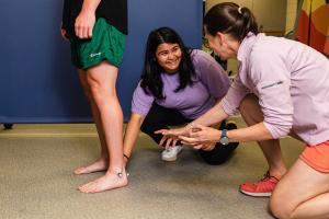 Faculty member is kneeling down demonstrating to a student how to attach a sensor to someone's leg