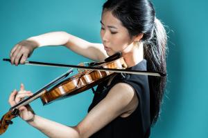 a violinist in a black sleeveless shirt plays a violin against a blue background