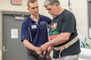 male physical therapy student helps an older man holding a small weight