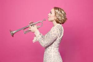a woman holds a trumpet on a pink background