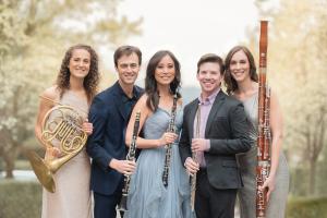 five people stand smiling and holding wind instruments