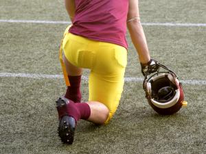 A football player in yellow and red kneels on the field