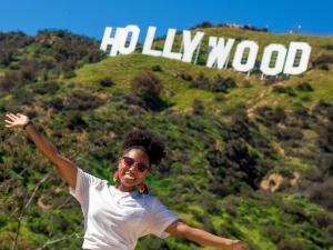 Young woman posing with arms held wide beneath the Hollywood sign.