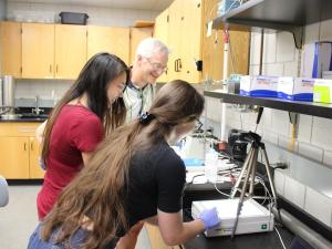 two students and a faculty look at a gel on the lab bench