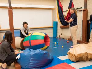 A group of faculty and students are in the occupational therapy clinic with play mats working with a child who is playing