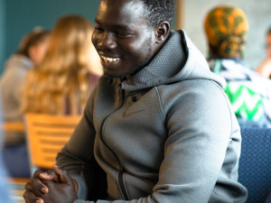 a student of color smiling, sitting down in a gray nike hoodie enjoying a conversation.