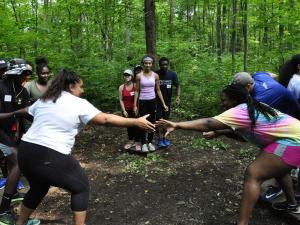 A group of students at a ropes course helping each other complete a challenge