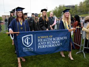 Two students are carrying a banner at graduation for the School of Health Sciences and Human Performance