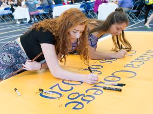 two women sign a banner that reads Ithaca College class of 2020