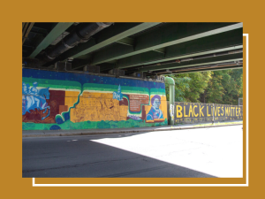 A colorful mural of a Frederick Douglas and Black Lives Matter under a bridge in Ithaca, New York, the sun is shining.