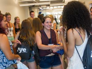 A student in a maroon tank top is shaking the hand of a new student to campus welcoming them.