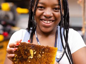 A student with long braided hair is hold a honeycomb up to the camera.