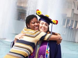 A graduate and friend hug in front of the fountains