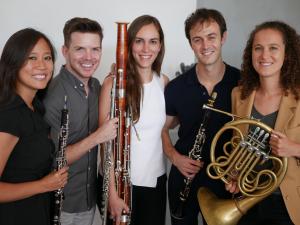 5 people stand smiling and holding wind instruments