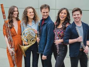 Five people stand smiling and holding wind instruments