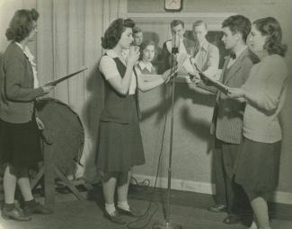 Black-and-white photo of students standing around a microphone.