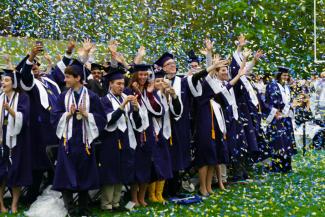 Graduates in caps and gowns celebrating with confetti.