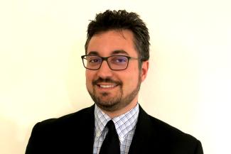 A bearded man wearing glasses and a business suit