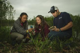 Three young people collect pond water in vials