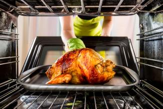A person removing a chicken from an oven