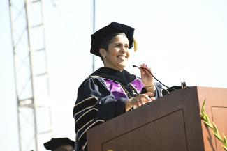 A woman in academic regalia speaking at a podium
