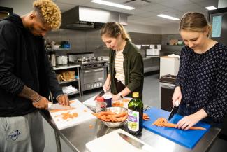 This is a picture of three students working in the food and nutrition lab. Each of them is standing at the kitchen island and they are chopping carrots.