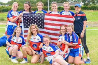 A group of women in athletic uniforms pose with the U.S. flag