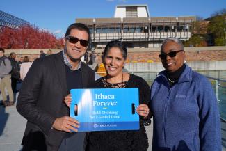 Three people pose with a sign that says Ithaca Forever