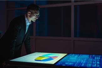 A man in a suit looks down at graphs on a monitor