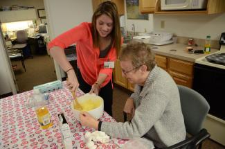 a student works with a senior citizen to mix together baking ingredients