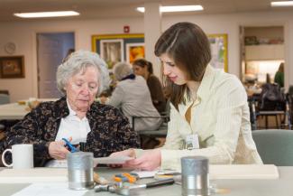 A student works with a senior citizen on cutting a piece of paper