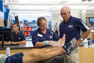An athletic training student works on a person's ankle under the guidance of an instructor