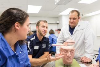 Two students and a faculty member examine a model of the human brain