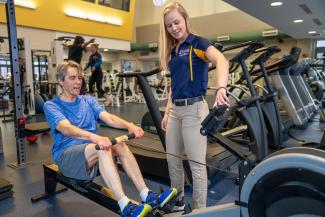 A Wellness Center member works out on a rowing machine under the guidance of a student trainer