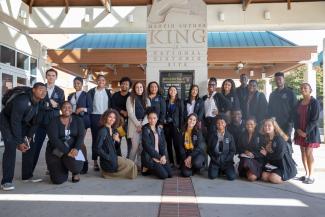 A group of 23 MLK Scholars in matching black jackets pose in front of an MLK museum in ATL