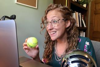 professor holds a tennis ball in front of a laptop
