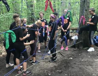 IC Leadership Scholars build their team skills while participating in a challenge course activity.   group of students outdoors on a spiderweb activity on a ropes course